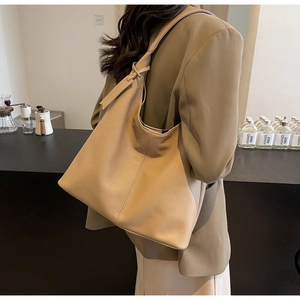 Detail view of large beige leather tote bag with wide shoulder strap on a model