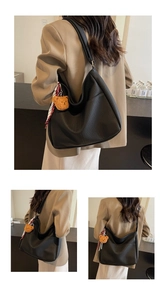 Detail of black large capacity hobo bag featuring litchi grain texture and a plush bear charm
