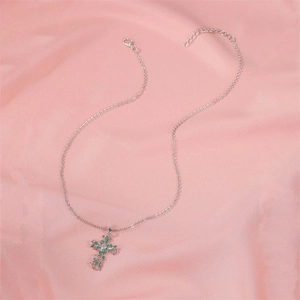 Silver cross necklace with green leaf vine and crystal pendant on pink silk fabric