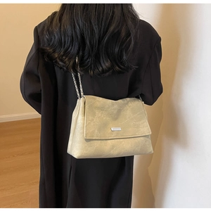 Detail of a beige suede chain tote bag shown on a model wearing a black winter coat