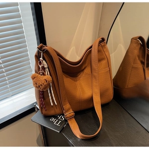 Detail of a brown textured faux leather tote bag with a cute plush bear charm decoration