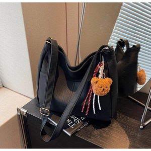 Detail of black pebbled leather tote bag with wide strap and plush bear charm accent