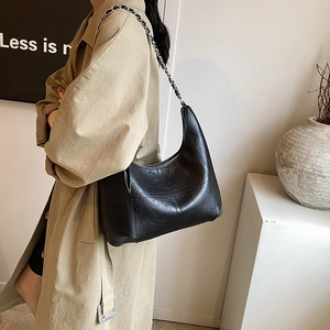 Minimalist black leather hobo bag with metal chain strap displayed in a modern lifestyle scene