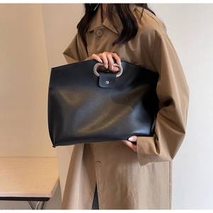 Detail of minimalist black leather handbag with unique oval metal cutout handle for work