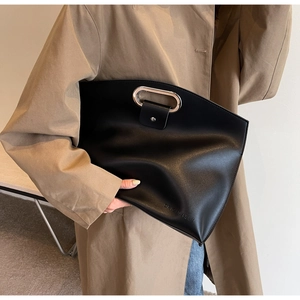 Detail of matte black leather tote bag featuring a silver oval handle and logo engraving