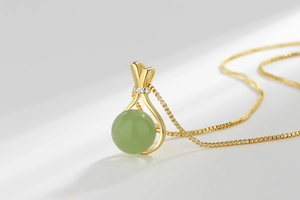 Macro view of a gold-tone lucky bag necklace with a green gemstone and tiny diamonds