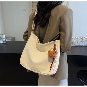 Detail of off-white large hobo bag with teddy bear charm worn by model in a modern cafe