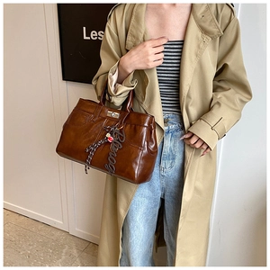 Detail of vintage brown tote bag with metal clasp and decorative charm on beige trench coat