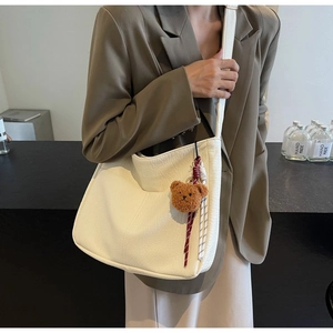Detail of cream white faux leather tote with brown plush bear and rope tassel