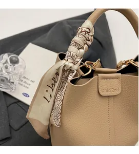 Detail of lychee textured leather bucket bag with silk scarf handle and gold buckle