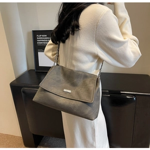 Chic dark grey tote bag with metal chain strap worn by a model in a minimalist room