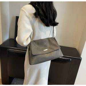 Detail of dark grey faux leather tote bag with silver chain strap and metal logo plaque
