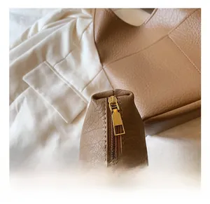Close-up of golden metal zipper hardware on brown lychee texture leather tote bag
