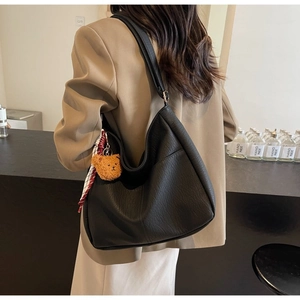 Detailed side view of black textured tote bag with teddy charm and plaid scarf on model
