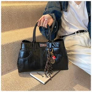 Close-up of black glossy shoulder bag with silver turn-lock and decorative charm