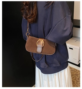 Detail of a brown suede baguette bag featuring a large gold buckle and leather trim