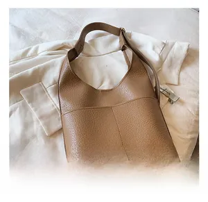 Detail of tan lychee grain leather tote bag with wide strap on a white blazer