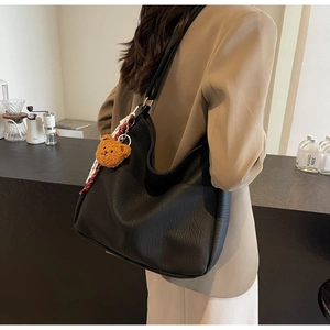 Detail of black pebbled leather tote bag with teddy bear charm shown on model