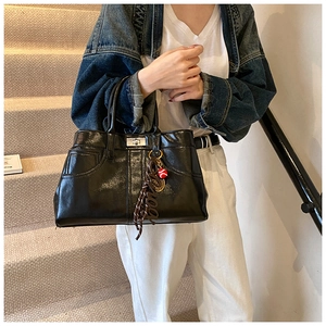 Detail of glossy black leather tote with silver clasp and braided tassel charm