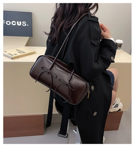 Detail of dark brown glossy leather underarm bag featuring decorative double bows