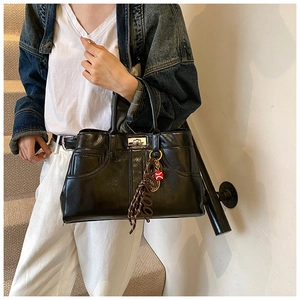 Close-up of black glossy leather tote bag with silver turn-lock and stylish bag charm