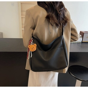 Detail of black pebbled leather hobo bag with a cute bear charm on a model's shoulder