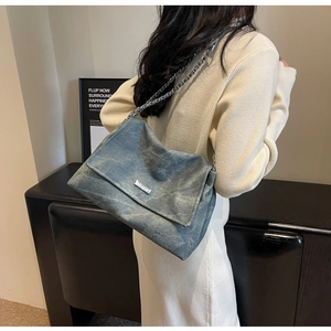 Detailed view of blue suede shoulder bag with metal chain strap worn by a model