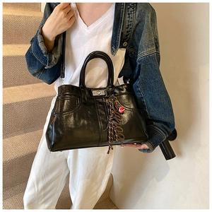 Close-up of black glossy leather shoulder bag with stitching and silver twist lock
