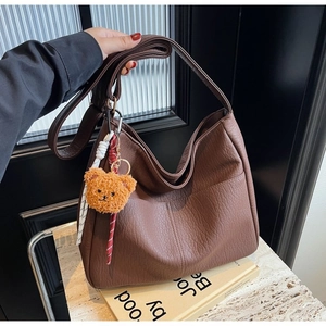 Detail of a brown lychee pattern hobo bag with a cute plush bear charm hanging on the side