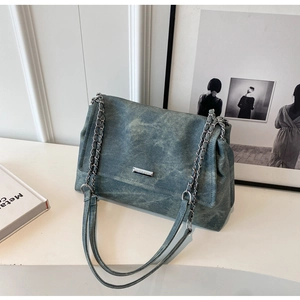Detail of blue denim shoulder bag with silver chain strap and rectangular metal logo plate