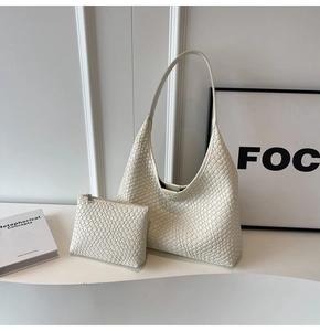 Detail of cream woven leather hobo bag and matching pouch on a minimalist white desk