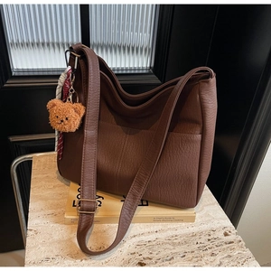 Detail of dark brown lychee texture leather tote bag with adjustable strap and bear charm