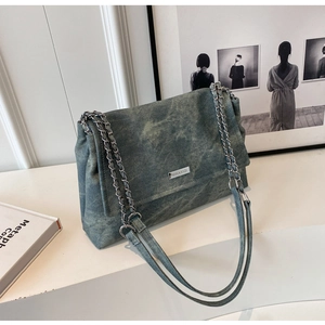 Close-up of vintage blue denim chain bag with silver metallic logo plate and leather strap
