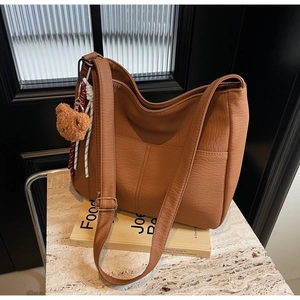 Detail of brown faux leather tote bag featuring a plush bear charm and adjustable strap