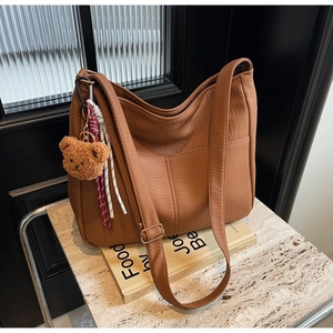 Detailed shot of brown pebble grain tote bag with bear charm on a stone stand
