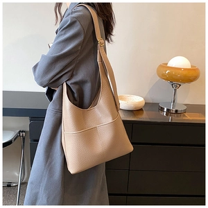 Detailed side view of a beige large tote bag made of pebbled leather on a female model