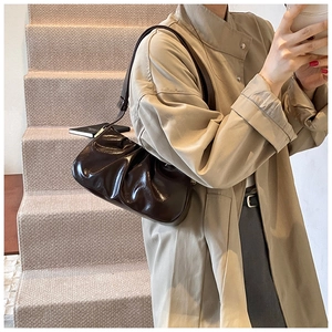 Detail of dark brown pleated croissant bag with shiny finish worn with a beige trench coat
