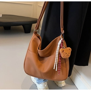 Detail of brown litchi pattern leather tote bag featuring a cute teddy bear pendant