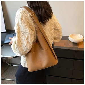 Detail view of brown pebbled leather tote bag featuring adjustable wide strap and side pocket