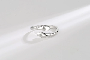 Macro detail of silver hugging hands ring featuring a polished adjustable open band