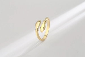 Dramatic studio lighting on golden adjustable hugging hands open ring design