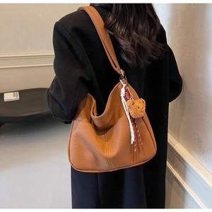 Close-up of brown textured leather tote with plush bear charm on a black wool coat