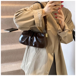 Detail of dark brown glossy cloud bag with pleated texture and adjustable gold buckle