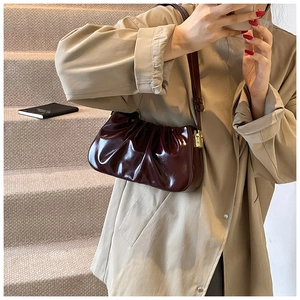 Close-up of pleated deep reddish-brown leather cloud bag with gold buckle detail