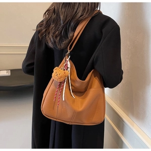 Close-up of caramel leather tote bag with lychee texture and cute bear pendant detail
