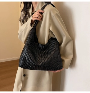 Close-up of a large black woven leather tote bag shown on a beige trench coat model