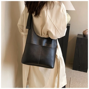 Close-up of black lychee texture leather tote bag on model wearing a beige trench coat