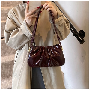 Detail of burgundy ruched cloud bag with glossy patent finish and gold hardware on model