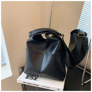 Close-up of black lychee grain leather tote bag with wide strap on a white book decor