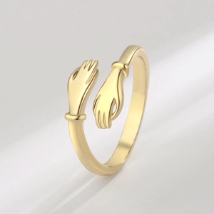 Minimalist golden hugging hands open ring with a polished metallic finish on grey background
